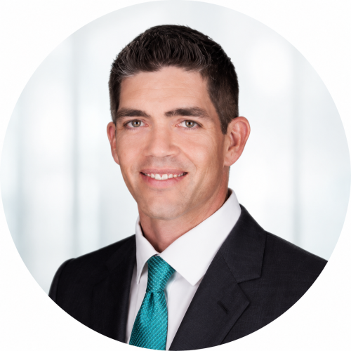 Professional circular headshot of a man wearing a dark business suit, white dress shirt, and teal tie. He is smiling directly at the camera against a soft, frosty white background with subtle ethereal blur effects. The portrait is clean, polished, and centered within a circular crop, conveying a professional and approachable appearance.